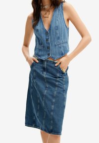 Jeansväst med vertikala ränder, djup V-hals, och fem knappar, parat med en matchande jeanskjol i knälängd med framträdande sömmar.