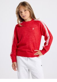 Roter Strickpullover mit hohem Kragen, versehen mit weißen Streifen an den Ärmeln und einem gerippten Saum. Weiche Textur mit einem kleinen Logodetail.