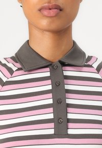 Randig polo t-shirt i grått, rosa och vitt. Har en grå krage och fem små bruna knappar upptill. Mjuk, ribbad textur.