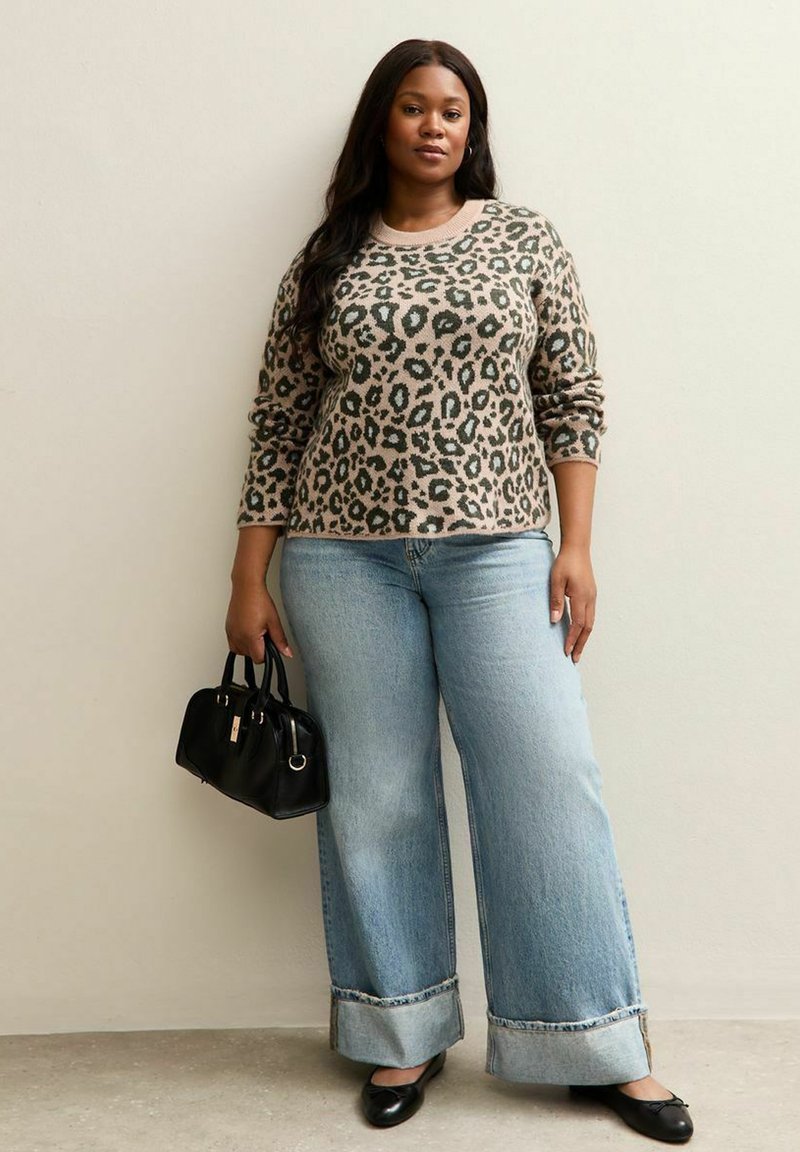 Beige en groene trui met panterprint, gecombineerd met lichtblauwe wijde jeans met opgerolde zoom. Model houdt een kleine zwarte handtas vast.