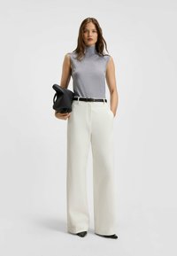 Top grigio senza maniche abbinato a pantaloni bianchi a gamba larga. Una cintura nera mette in risalto la vita e una borsa nera strutturata completa il look.