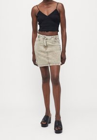 Black crocheted crop top and beige denim mini skirt. The skirt features classic five-pocket styling and a zipper closure. Black platform slides.