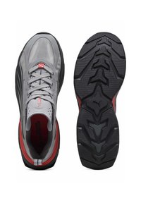 Chaussures de sport grises avec une tige en mesh, des accents rouges et une semelle extérieure en caoutchouc noir texturé présentant un motif de crampons distinctif.