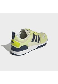 Zapatillas deportivas en amarillo claro y azul marino, con materiales de malla y ante, tres franjas diagonales, cuello acolchado y suela de goma.