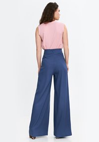 Spodnie w kant, o wysokim stanie i szerokich nogawkach, wykonane z granatowej tkaniny, zestawione z różową bluzką bez rękawów. Gładka struktura, minimalistyczny design i dyskretne zapięcie z tyłu.