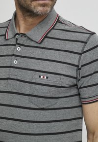 Gråstripet polo-skjorte med svart og rød krage, med en brystlomme med en liten trikolor stripe detalj og tre knapper.