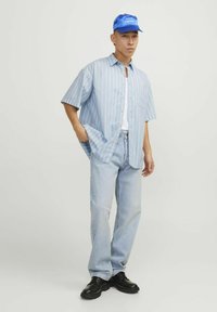 Camisa de botones en azul claro con rayas verticales, combinada con jeans azul claro y zapatos negros. Una gorra azul completa el conjunto.