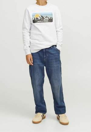 Grijze sweatshirt met een grafisch ontwerp van bergen en een zon, gecombineerd met losse blauwe denim broek en beige sneakers.