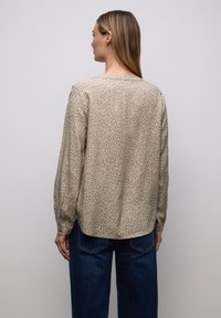 Blouse beige à manches longues avec un imprimé animalier subtil, dotée d'un col arrondi et d'une texture douce. Associée à un pantalon en jean foncé.