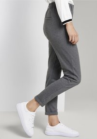 Spodnie w czarno-białym wzorze w jodełkę z tapered nogawkami, posiadające elastyczny pasek i boczne kieszenie, w połączeniu z białymi sneakersami.