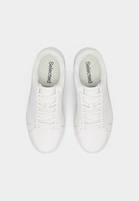 Paire de baskets blanches à lacets avec la marque "Selected" sur des semelles intérieures rembourrées, vues de dessus sur un fond uni.