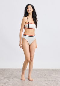 Σετ μπικίνι δύο τεμαχίων σε κρεμ χρώμα, με κόκκινες και μαύρες οριζόντιες ρίγες. Το πάνω μέρος είναι στυλ bandeau, το κάτω μέρος έχει ψηλή μέση. Ομαλή υφή.