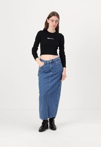 Schwarzes, cropped Langarmoberteil mit gerippter Textur und Logo. Hochtaillierter, blauer Jeans-Maxirock mit vorderer Naht und Taschen an den Seiten. Schwarze Ankle-Boots.