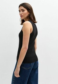 Svart ribbad linne med en åtsittande design, utrustad med breda axelband. Matchat med högmidjade blå jeans för en avslappnad look.