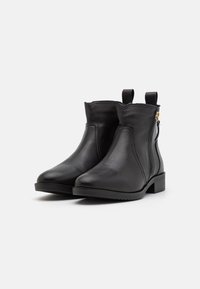 Bottines noires en cuir avec une texture lisse, talon bloc bas, fermeture éclair latérale pour un enfilage facile, et languettes pour faciliter la mise.