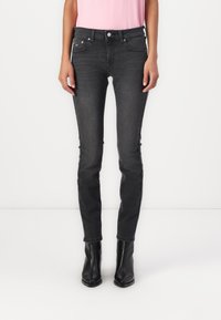 Jeans ajustados en denim gris oscuro, con un diseño clásico de cinco bolsillos y una cremallera con botón. Combinados con botas de tobillo negras.