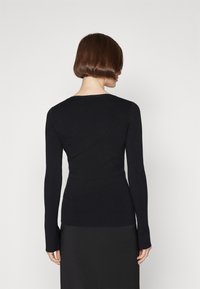 Sort ribbet strikket langærmet top med rund halsudskæring, tætsiddende silhuet og forlængede manchetter, parret med en elegant sort nederdel.