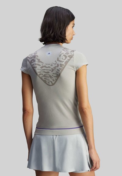 Vaaleanharmaa urheilupaita lyhyillä hihoilla, jossa on selässä kuvioitu kolmionmuotoinen kuvio ja violettti raita helmassa.