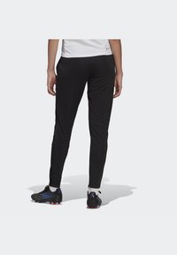 Black athletic pants with a fitted design, featuring a smooth texture and side zippers, paired with black and blue sports shoes.