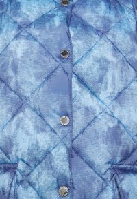 Casaco puffer acolchoado azul com um acabamento texturizado, apresentando um padrão em diamante e botões de pressão prateados.