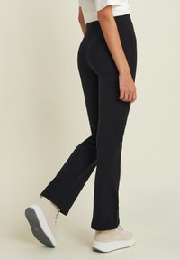 Pantaloni neri su misura con vestibilità slim, dotati di tasche laterali e una texture liscia, abbinati a sneakers beige.