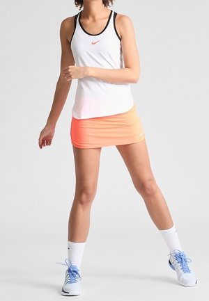 Débardeur blanc avec des accents noirs et un logo Nike orange, associé à une jupe orange. Des chaussures de sport bleues et des chaussettes blanches complètent la tenue.