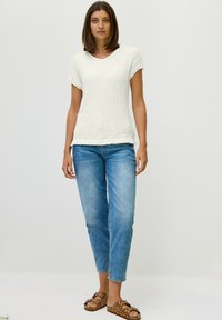 Witte, gemêleerde trui met V-hals, gecombineerd met lichtblauwe, iets tapered jeans en bruine sandalen met geperforeerd design.