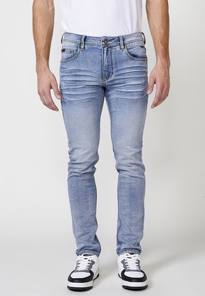 Jeans din denim de culoare albastru deschis, cu o croială slim, prezentând zone decolorate, cinci buzunare și un sistem de închidere cu nasture. Asortați cu adidași negri și albi.