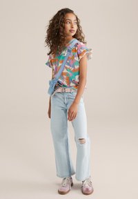 Camisa de manga corta colorida con un patrón tropical, jeans de tiro alto azul claro con una rodilla rasgada y zapatillas rosas con cordones blancos.