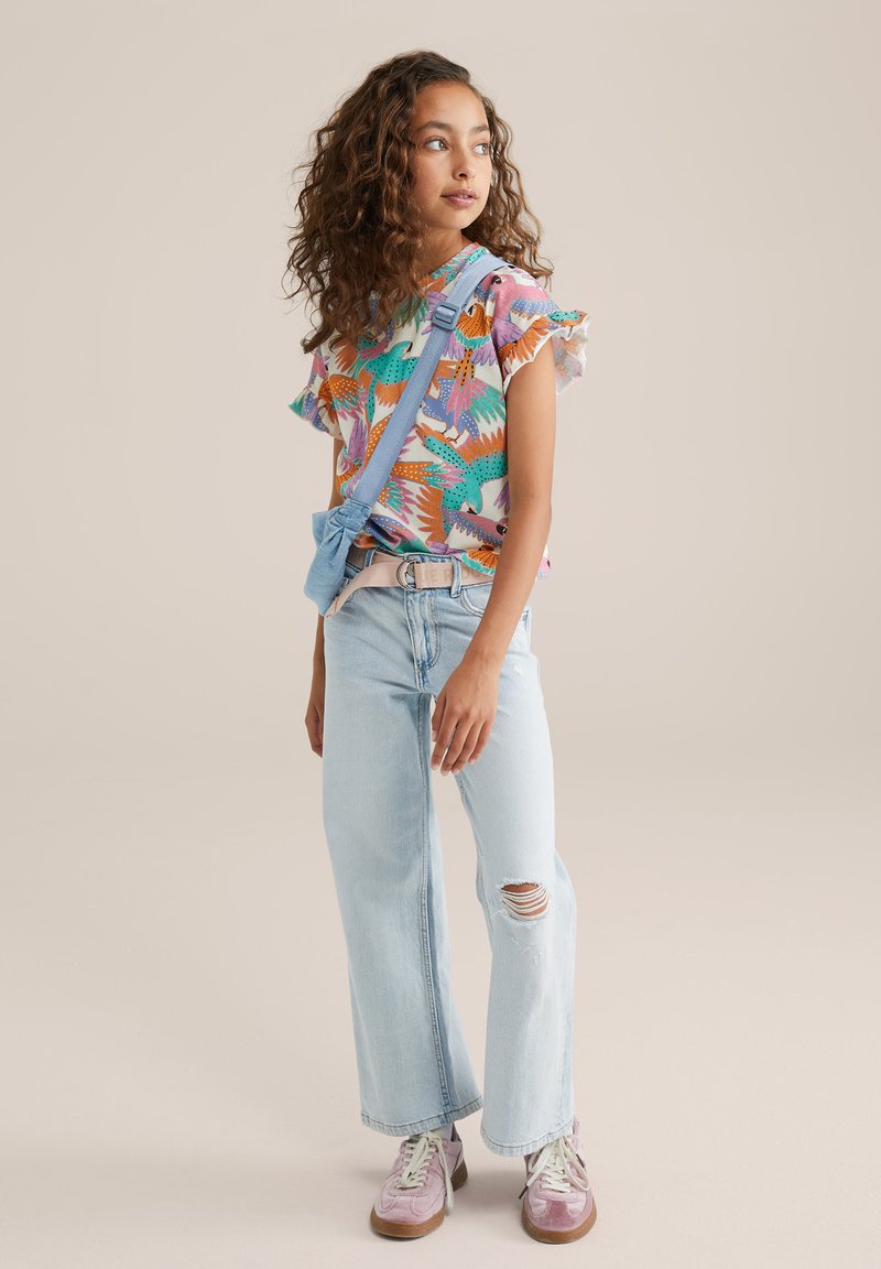 Camisa de manga corta colorida con un patrón tropical, jeans de tiro alto azul claro con una rodilla rasgada y zapatillas rosas con cordones blancos.
