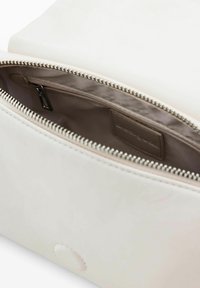 White leather bag interior with a zippered closure, smooth texture, and a small label stitched inside. Visible stitching and sleek design.