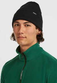 Sort ribbet beanie med O'Neill-logo. Blød tekstur. Modellen har en grøn fleecejakke med lynlås og høj krave samt kontrastfarvet lynlås på.