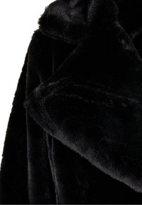 Gros plan sur un tissu en fausse fourrure noire douce avec un col plié et une texture moelleuse.