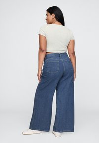 Traperice širokih nogavica s visokim strukom, tamnoplave boje. Imaju dva stražnja džepa i mekan, svijetlosivi prigodni top. Ležerna obuća.