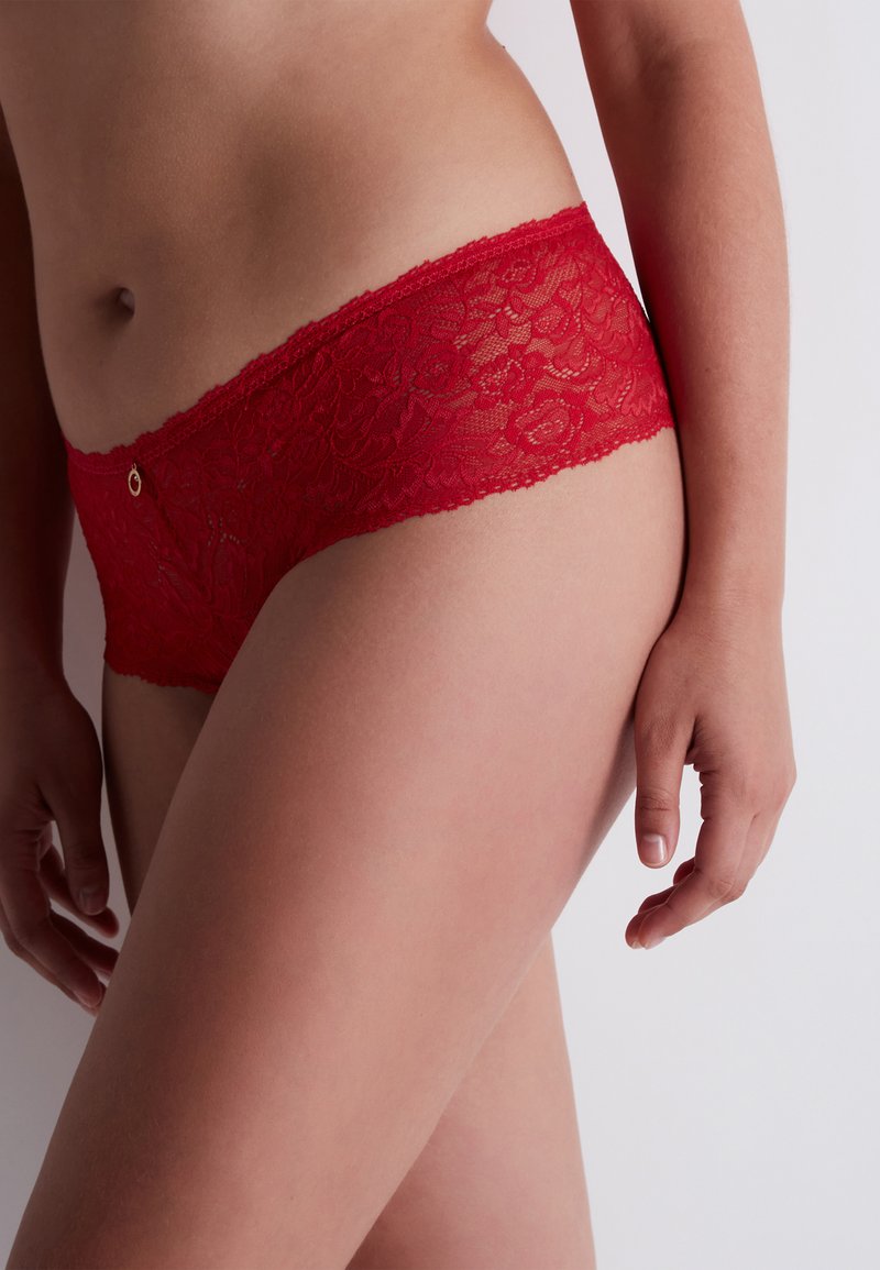 Rode kanten onderbroek met een bloemenpatroon en geschulpte randen, voorzien van een kleine ronde gouden accent bij de tailleband. Zachte textuur, hipster stijl.
