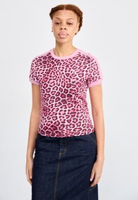 Korte mouwen roze t-shirt met zwart en donkerroze luipaardprint, met een ronde hals en contrasterende roze afwerking. Draag het met een spijkerrok.