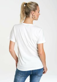 White short-sleeve t-shirt made of soft fabric, featuring a round neckline, smooth texture, and a classic fitted shape. Worn with blue jeans.