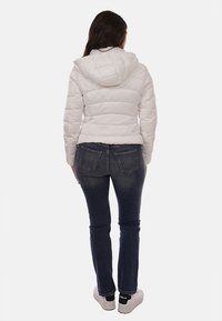 Giacca imbottita bianca con cappuccio e design trapuntato, abbinata a jeans slim-fit blu scuro e sneakers bianche. Vista da dietro.