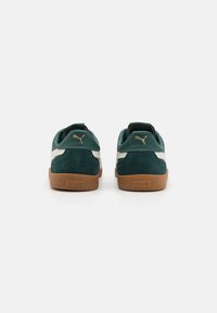 Sneaker in camoscio e pelle verde con suola in gomma color tan, caratterizzate da un motivo a strisce bianche e dal logo Puma dorato sul tallone e sul lato.
