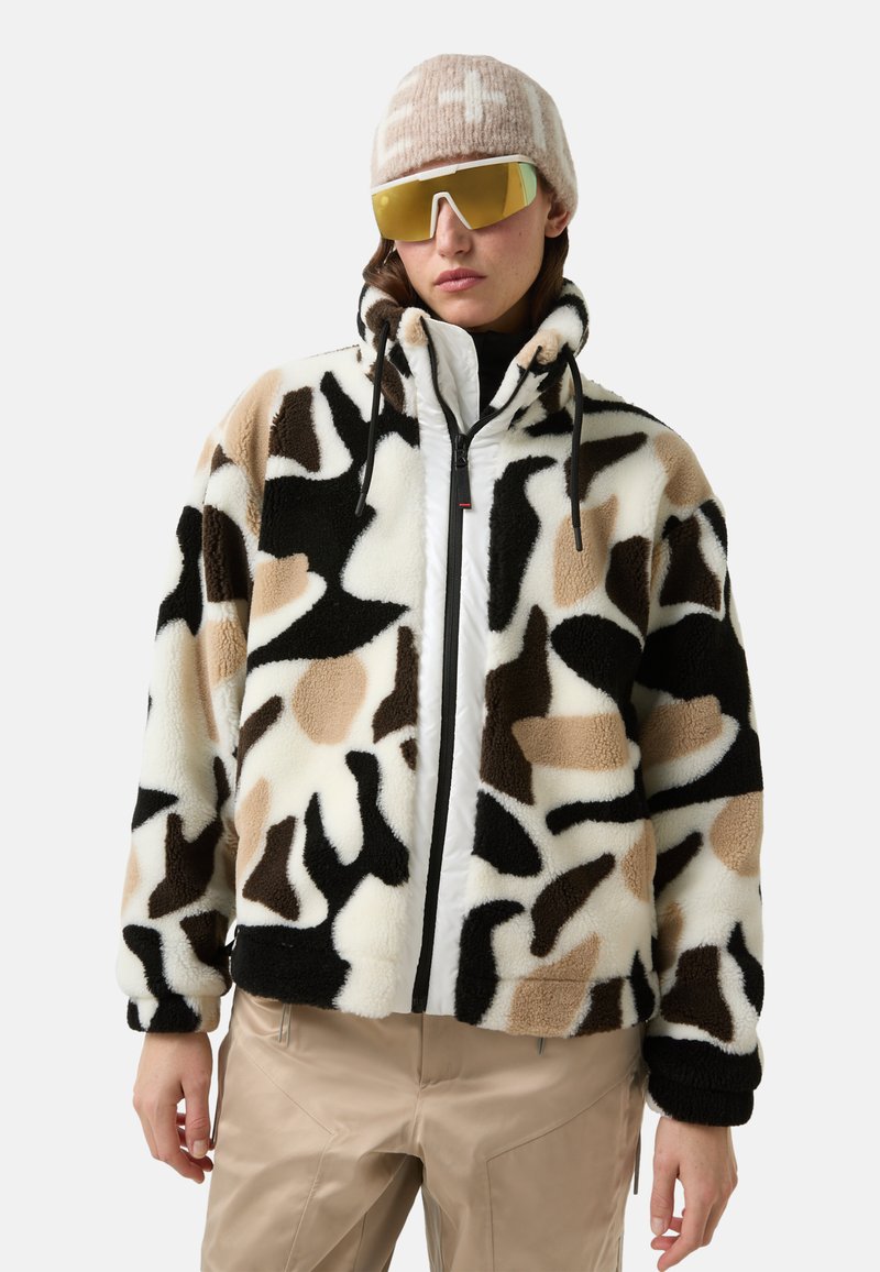 Pluizige jas met abstract zwart, beige en wit patroon, ritssluiting aan de voorkant en verstelbare capuchon. Gecombineerd met beige broek en accessoires.