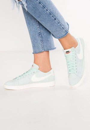 Baskets en daim vert menthe clair avec des accents blancs, présentant un design à lacets et une semelle texturée, portées avec un jean court en denim effiloché.