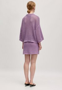 Lavendel haak gebreide set met een losse, oversized top met brede mouwen en een bijpassende aansluitende rok, beide met een open weefpatroon.