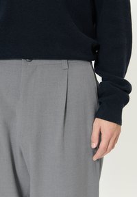 Meresinist tekstuuriga kampsun, mida täiendab heledat halli volditud pükse, millel on nööpidega kinnis ja küljetaskud. Sile kangas ning lõdvestunud lõige.