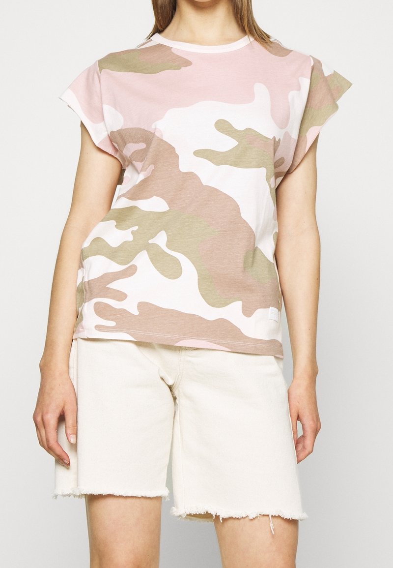 Světle růžové maskáčové tričko s krátkým rukávem vyrobené z měkké bavlny. Spárováno s roztrhanými bílými denimovými šortkami.