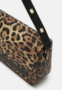 Pieni suorakaiteen muotoinen käsilaukku, jossa on ruskean ja mustan leopardikuvion, musta säädettävä olkahihna kullanvärisillä niiteillä ja musta korostuspaneeli edessä.