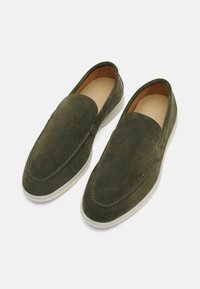 Scarpe slip-on verde in suede con punta arrotondata, dettagli di cucitura e suola in gomma bianca a contrasto. L'interno è foderato in color testa di moro.