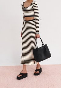 Sorte og creme stribede ribbede strik to-delt sæt, der indeholder en cropped langærmet top og en tætsiddende nederdel. Kombineret med en sort tote bag og chunky sandaler.