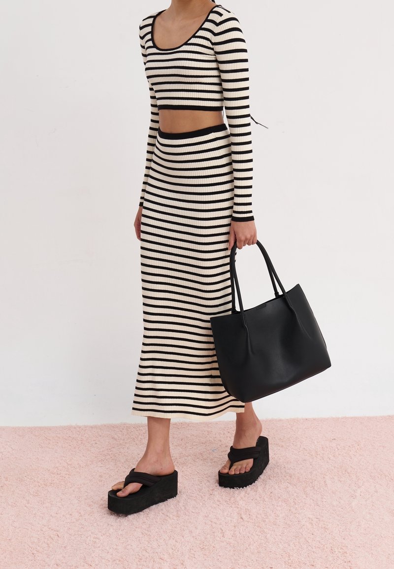 Sorte og creme stribede ribbede strik to-delt sæt, der indeholder en cropped langærmet top og en tætsiddende nederdel. Kombineret med en sort tote bag og chunky sandaler.