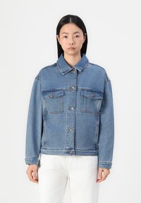 Veste en denim bleu avec un col, des poches avant et une fermeture à boutons. Présente une coupe décontractée et un lavage bleu clair.
