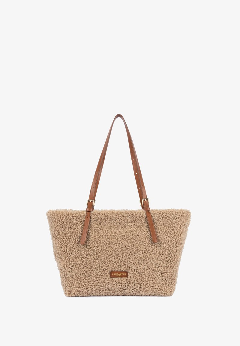 Sac cabas beige texturé avec des anses en cuir marron réglables et un petit patch logo Lancaster Paris au centre à l'avant.